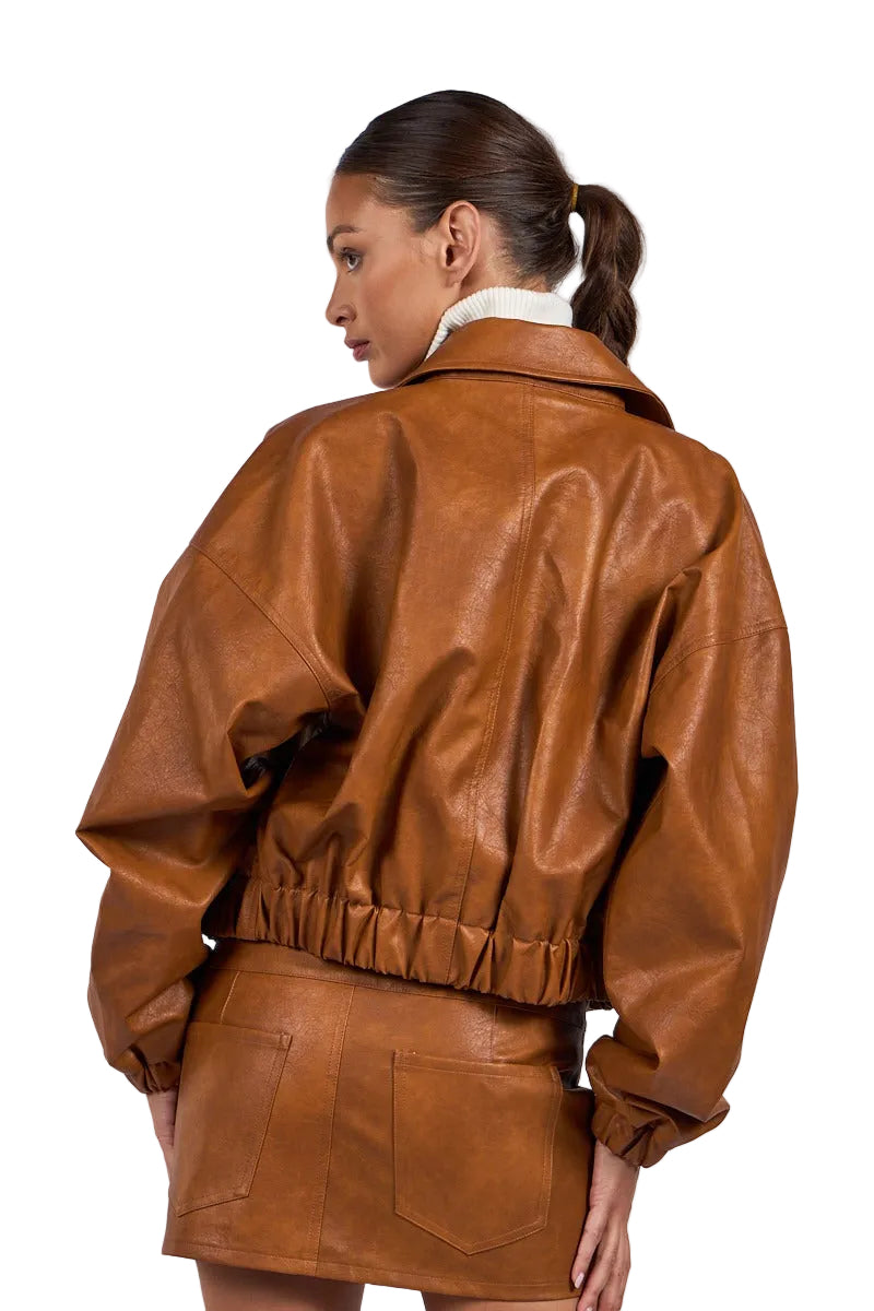 A woman shown from the back wearing a brown faux-leather jacket and matching mini skirt against a light gray studio background.