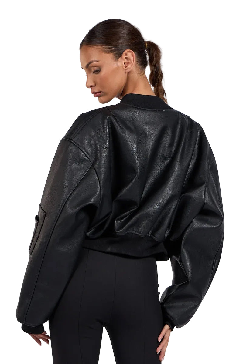 A woman shown from the back wearing a black faux-leather bomber jacket with oversized sleeves and black pants, photographed against a light gray studio background.